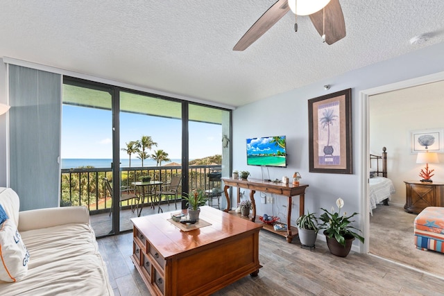 living area with wood finished floors, a textured ceiling, a wall of windows, a ceiling fan, and baseboards