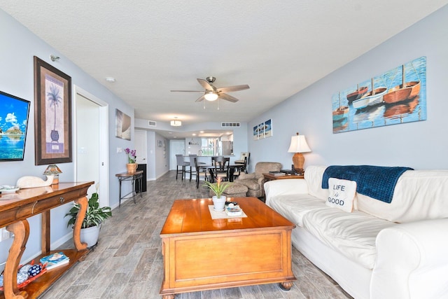 living area featuring light wood finished floors, a textured ceiling, visible vents, and a ceiling fan