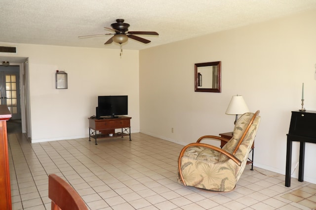 living area featuring light tile patterned floors, ceiling fan, visible vents, and a textured ceiling