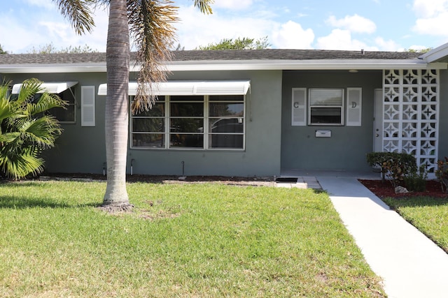 view of front of property with a front yard, stucco siding, and roof with shingles