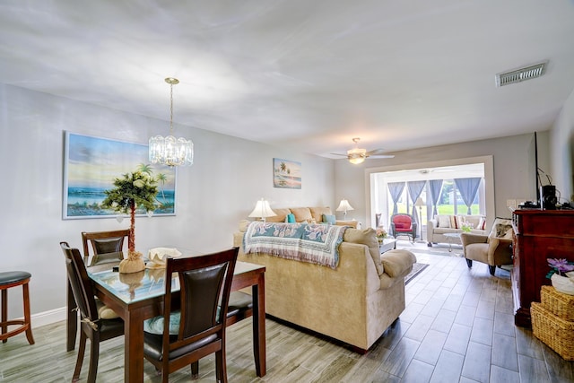living room featuring baseboards, visible vents, wood finished floors, and ceiling fan with notable chandelier