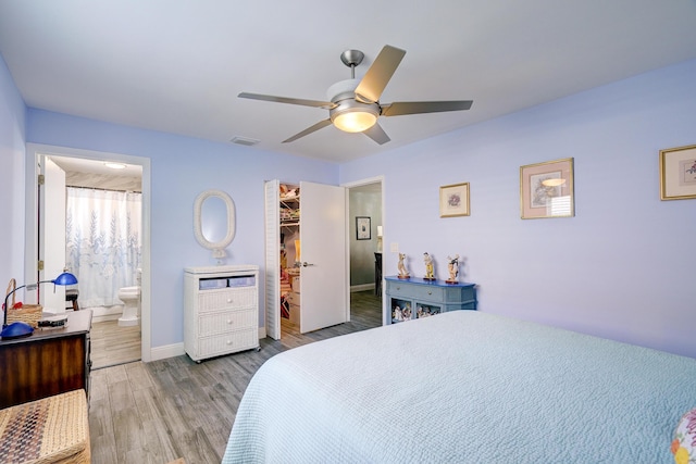 bedroom with wood finished floors, a ceiling fan, a walk in closet, visible vents, and baseboards