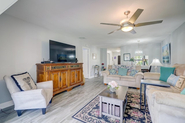 living room with light wood-style floors, baseboards, and ceiling fan with notable chandelier