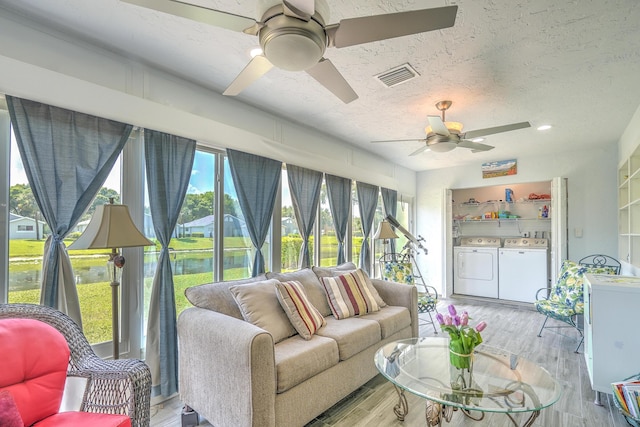 sunroom with a water view, wood finished floors, a textured ceiling, visible vents, and independent washer and dryer