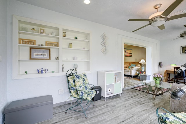 living area with a textured ceiling, built in features, wood finished floors, and a ceiling fan
