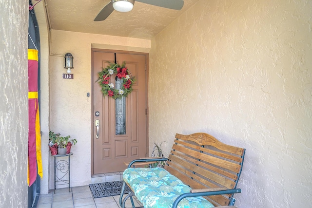 entrance to property with ceiling fan and stucco siding