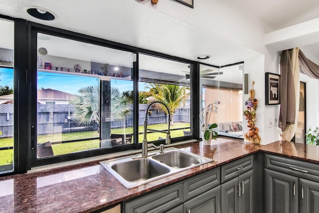 kitchen with a sink, gray cabinetry, dark stone countertops, and plenty of natural light