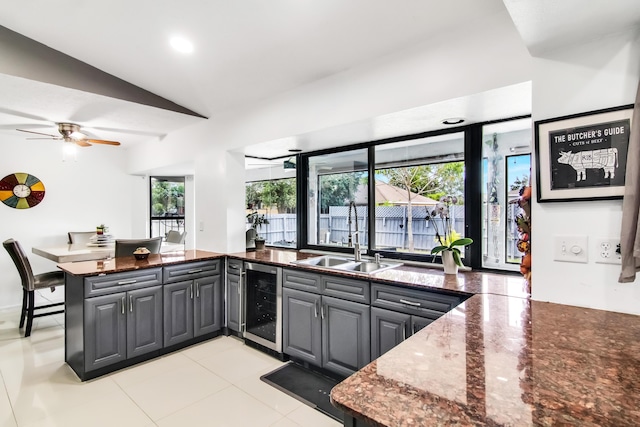 kitchen with a sink, a peninsula, lofted ceiling, gray cabinets, and beverage cooler