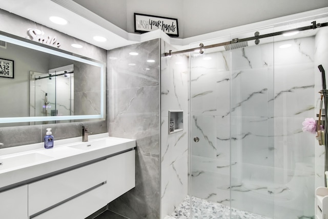 full bath with double vanity, tile walls, a marble finish shower, and a sink