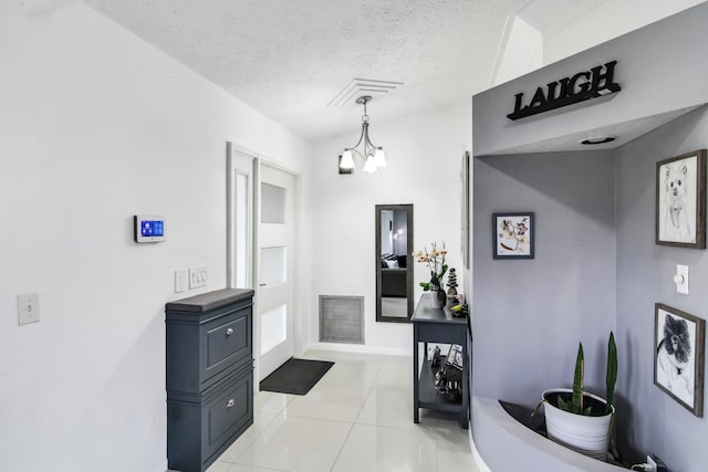 hallway with a textured ceiling, light tile patterned floors, baseboards, visible vents, and a chandelier