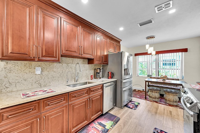 kitchen with a sink, stainless steel appliances, light wood finished floors, tasteful backsplash, and brown cabinetry