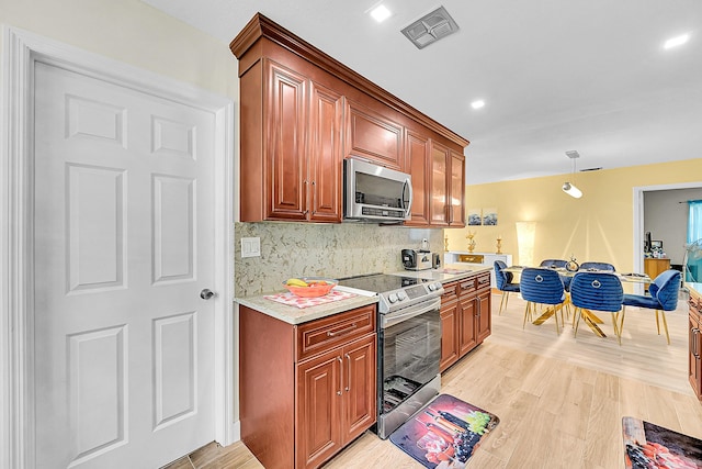kitchen with appliances with stainless steel finishes, light countertops, light wood-style floors, backsplash, and decorative light fixtures