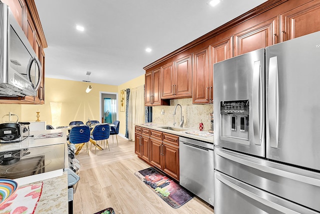 kitchen featuring stainless steel appliances, a sink, light countertops, light wood-style flooring, and decorative backsplash