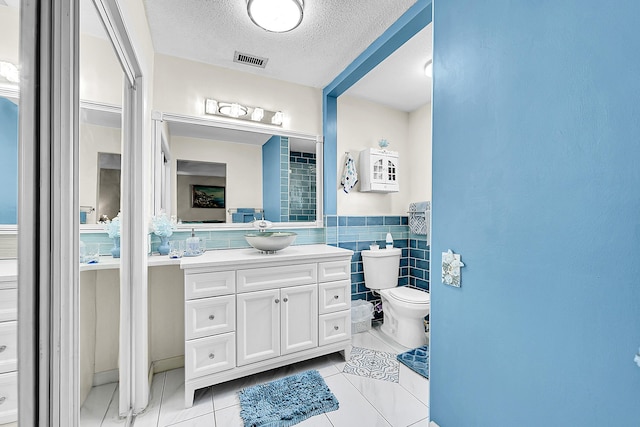 bathroom with toilet, tile patterned flooring, vanity, a textured ceiling, and tile walls
