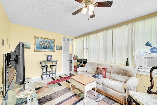 living area with a ceiling fan, a textured ceiling, cooling unit, and baseboards