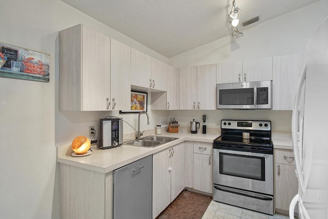 kitchen with stainless steel appliances, a sink, light countertops, lofted ceiling, and light tile patterned floors