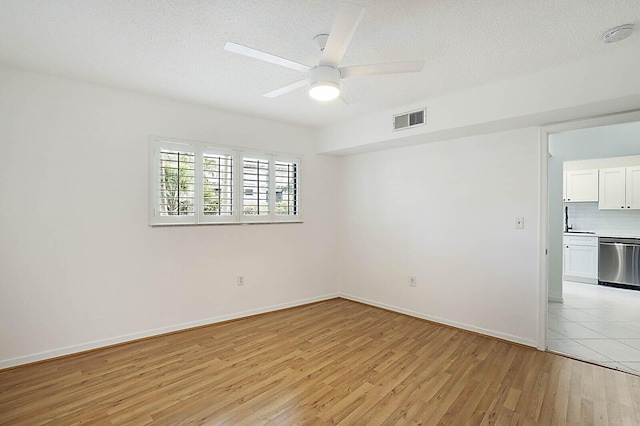 spare room with light wood finished floors, a ceiling fan, a textured ceiling, baseboards, and a sink