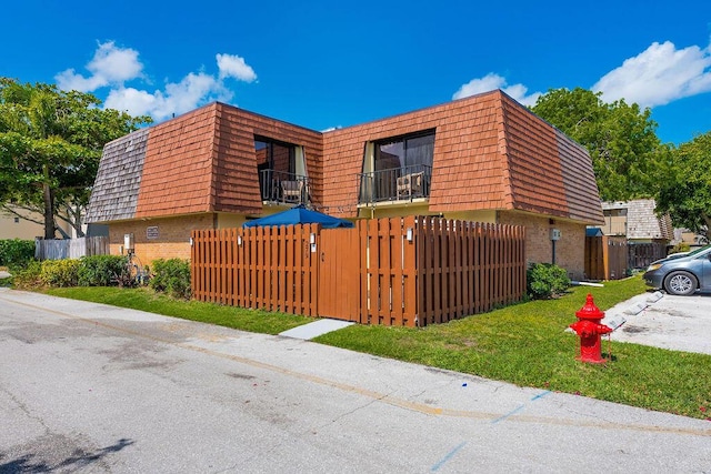 view of home's exterior featuring brick siding, mansard roof, a fenced front yard, and a gate