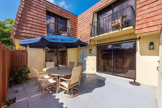 view of patio / terrace with a balcony, outdoor dining area, and fence