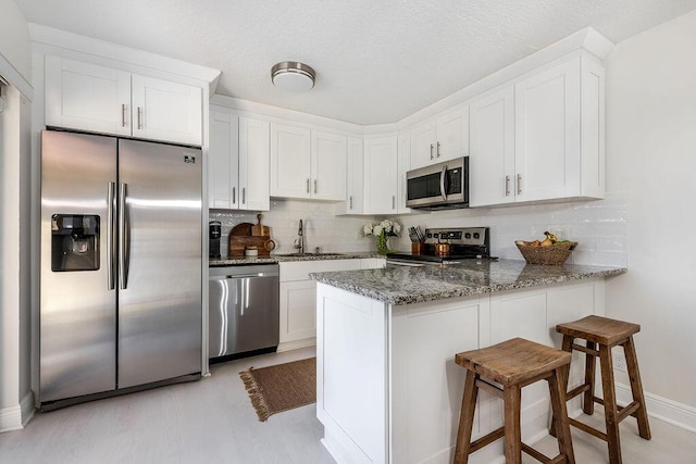 kitchen with appliances with stainless steel finishes, a sink, dark stone counters, a peninsula, and white cabinetry