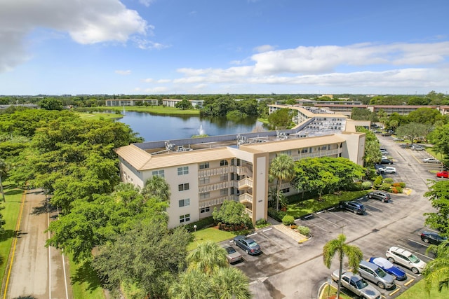 drone / aerial view of a large body of water, apartment complex / building, and a tree filled landscape