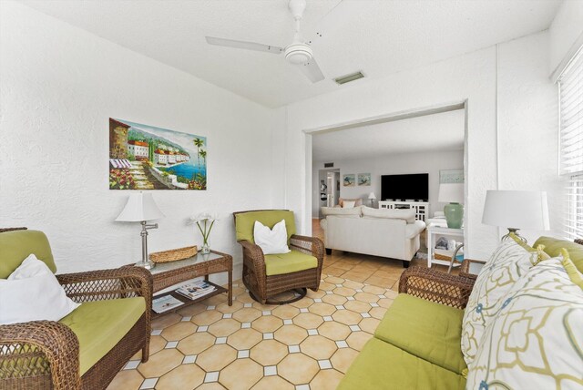 living area featuring ceiling fan and a textured wall