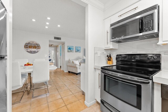 kitchen with stainless steel appliances, white cabinetry, backsplash, light countertops, and ornamental molding