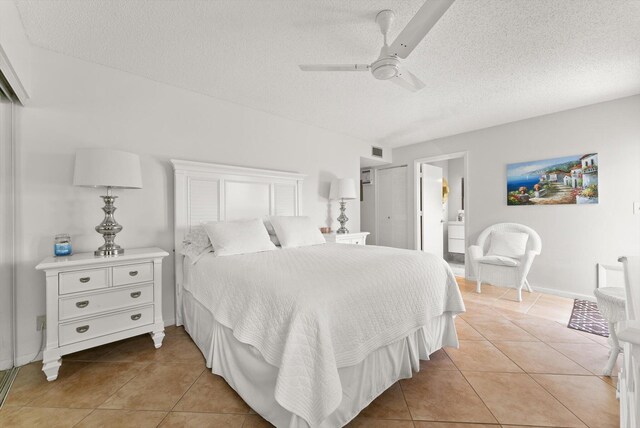 bedroom featuring light tile patterned floors, a textured ceiling, ceiling fan, baseboards, and ensuite bathroom