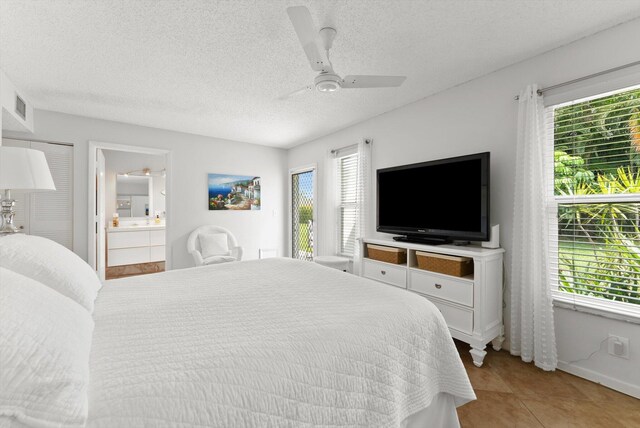 bedroom with multiple windows, a textured ceiling, ensuite bath, a ceiling fan, and light tile patterned floors