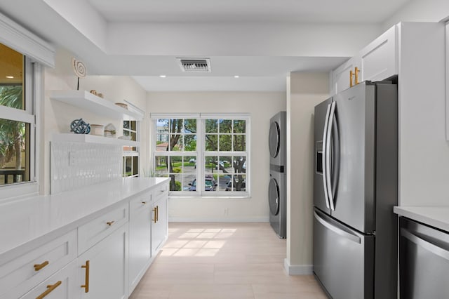 kitchen featuring stainless steel appliances, open shelves, visible vents, stacked washer and clothes dryer, and white cabinets