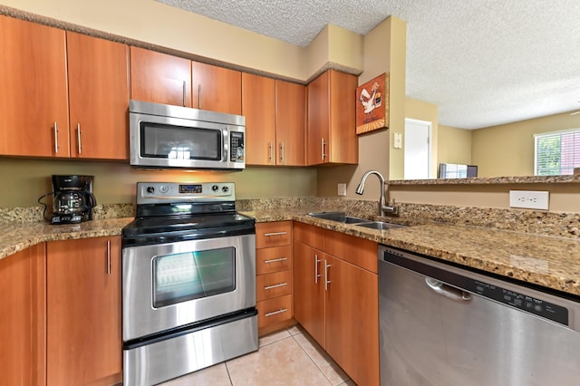 1125 Crystal Way Unit I, Delray Beach, FL 33444 - kitchen featuring stainless steel appliances, a sink, a textured ceiling, brown cabinetry, and light stone counters