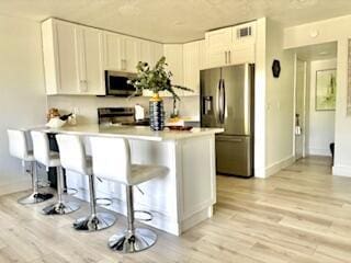 kitchen featuring a peninsula, stainless steel appliances, light wood-style flooring, light countertops, and a kitchen bar