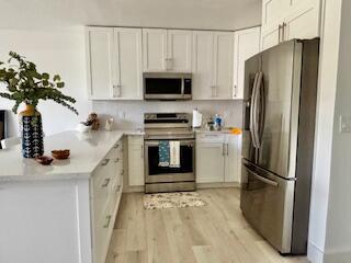 kitchen featuring a peninsula, white cabinetry, light wood-type flooring, light countertops, and appliances with stainless steel finishes