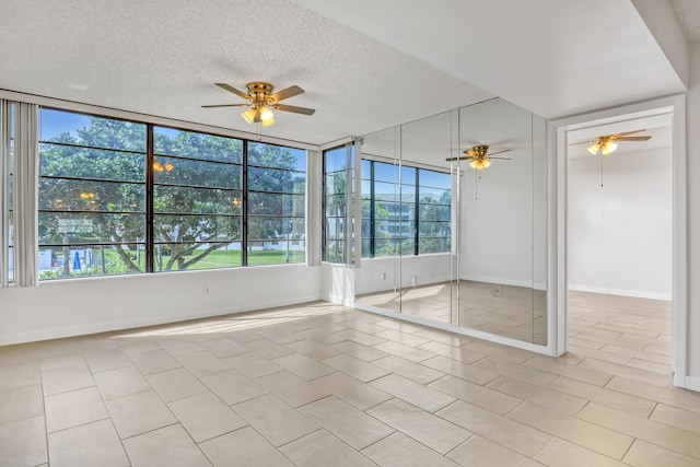 empty room featuring a textured ceiling, a wealth of natural light, baseboards, and a ceiling fan