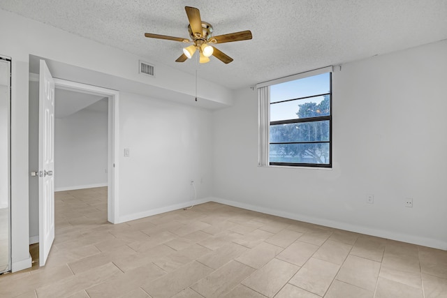 spare room featuring a textured ceiling, visible vents, baseboards, and ceiling fan