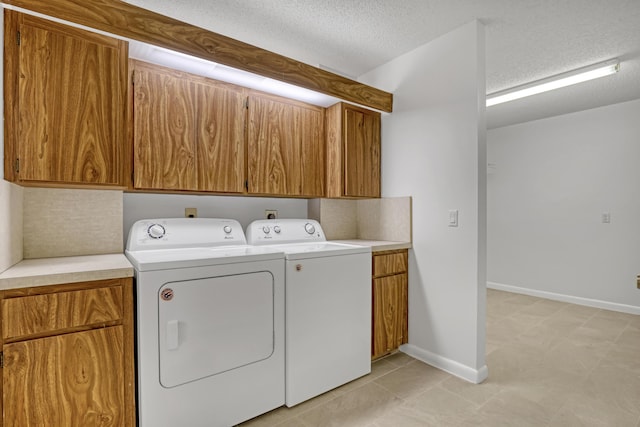 washroom with cabinet space, a textured ceiling, washer and dryer, and baseboards