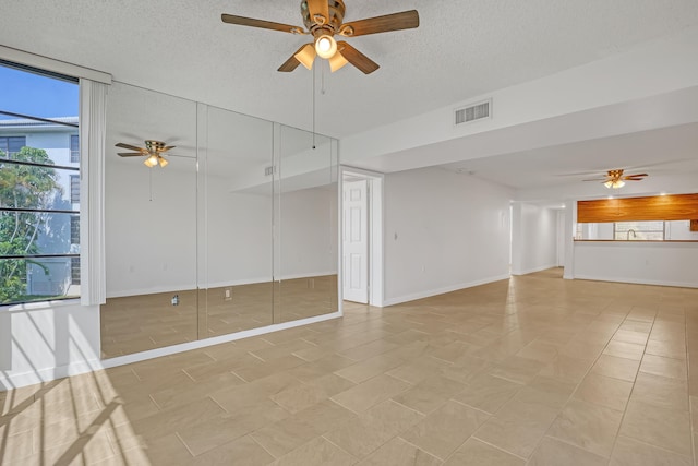 empty room featuring a textured ceiling, baseboards, a ceiling fan, and visible vents