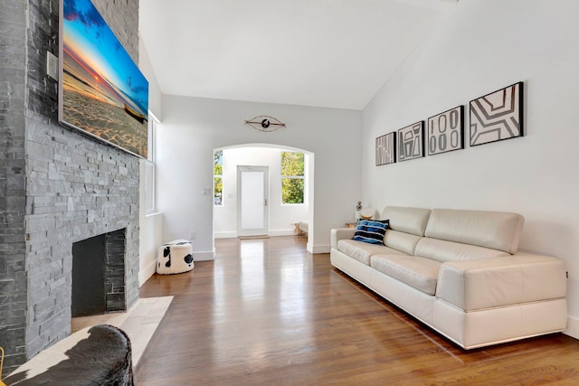 430 NE 121st St, Biscayne Park, FL 33161 - living area with baseboards, a stone fireplace, high vaulted ceiling, wood finished floors, and arched walkways