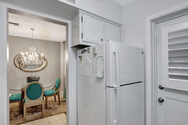 kitchen featuring freestanding refrigerator, a chandelier, light tile patterned flooring, and white cabinets