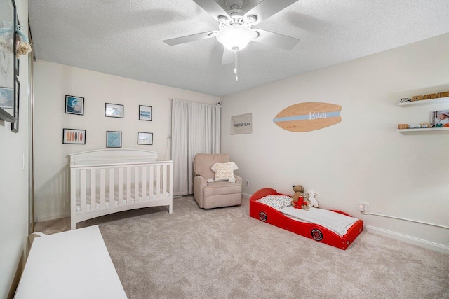 carpeted bedroom with ceiling fan, a textured ceiling, a nursery area, and baseboards