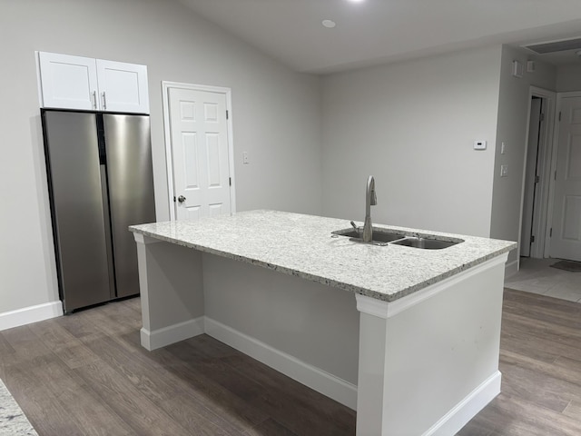 kitchen with freestanding refrigerator, a sink, wood finished floors, a kitchen island with sink, and lofted ceiling