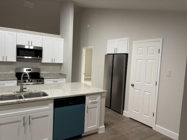 kitchen with appliances with stainless steel finishes, a sink, white cabinetry, wood finished floors, and light stone counters