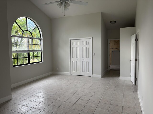 unfurnished bedroom featuring vaulted ceiling, a closet, light tile patterned flooring, baseboards, and ceiling fan