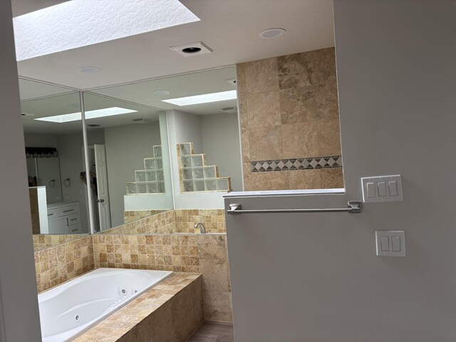 bathroom with a jetted tub, a skylight, and recessed lighting