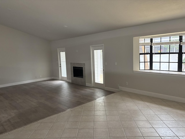 unfurnished living room with plenty of natural light, baseboards, a fireplace, and light wood-style floors