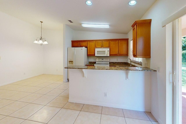 kitchen with lofted ceiling, brown cabinetry, white appliances, a peninsula, and dark stone countertops