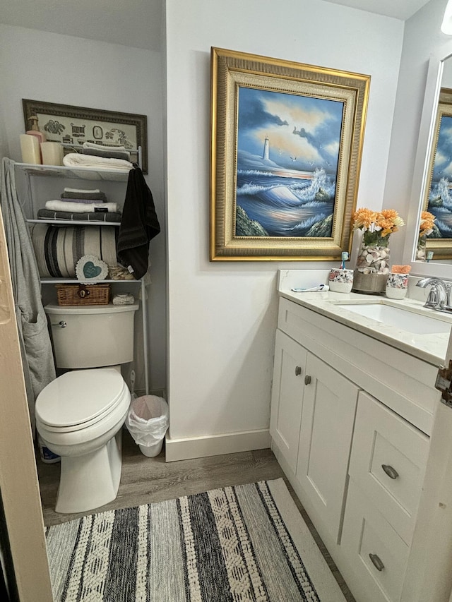 bathroom featuring baseboards, vanity, toilet, and wood finished floors