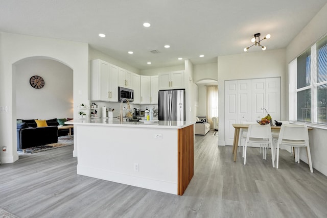 kitchen featuring light wood-style flooring, stainless steel appliances, recessed lighting, arched walkways, and light countertops