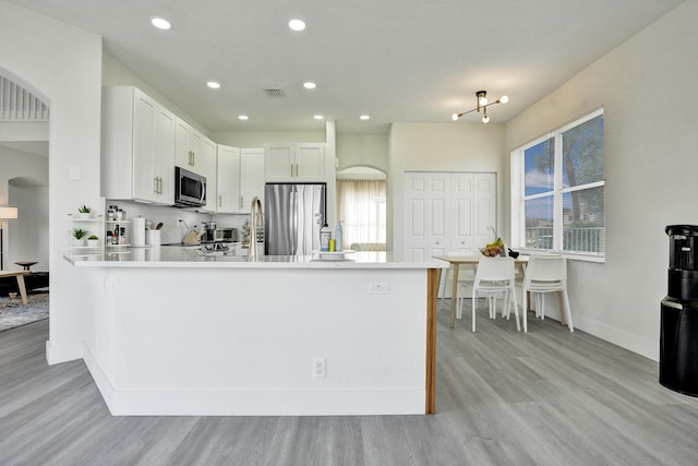 kitchen featuring a peninsula, appliances with stainless steel finishes, light wood finished floors, and arched walkways