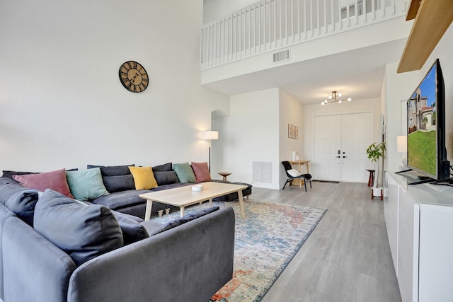 living room with light wood finished floors, an inviting chandelier, visible vents, and a high ceiling